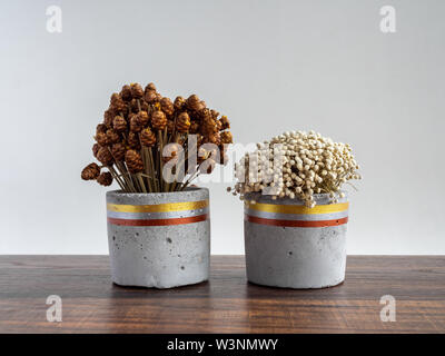 Wunderschön bemalte konkrete Pflanzmaschine mit getrockneten Blumen auf Holztisch auf weißem Hintergrund. Handgefertigte Zement Topf für Dekoration. Stockfoto