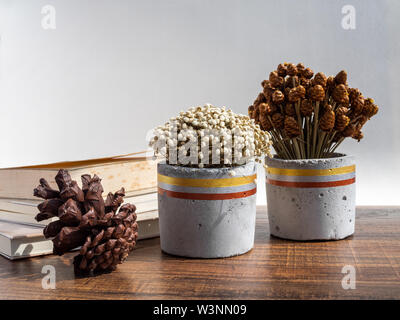 Wunderschön bemalte konkrete Pflanzmaschine mit getrockneten Blumen, natürliche Tannenzapfen und alte Bücher über Holz- Hintergrund. Handgefertigte Zement Topf für Dekoration. Stockfoto