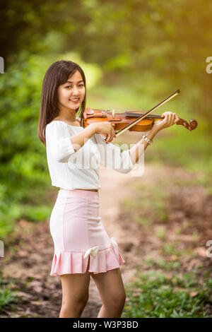 Asien Frau spielen Violine im Garten bei Sonnenschein Stockfoto