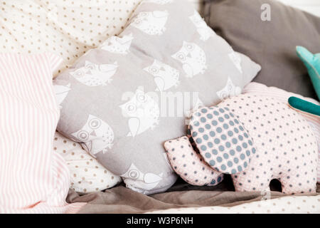 Soft baby Kissen auf dem Bett. Kissen mit gemalten Eulen und Plüschtier in Form eines Elefanten Stockfoto