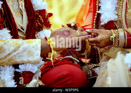 Braut mit Brautschmuck und Henna Dekoration auf ihre Hand legt Ring pflegt Finger auf traditionelle religiöse Zeremonie an einem hinduistischen Hochzeit Stockfoto