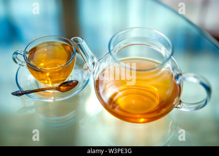 Transparentes Glas Tee Tasse und Becher mit Löffel auf Glas Tisch in starke Hintergrundbeleuchtung Stockfoto