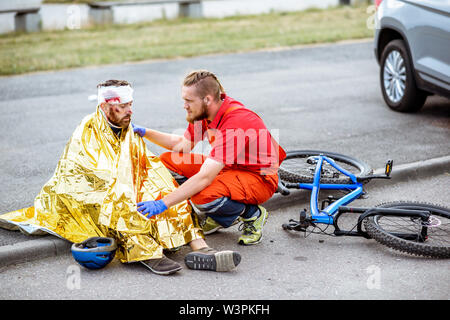 Ambluence Arbeiter, die verletzten Mann mit thermodecke, die Notfallversorgung nach dem Verkehrsunfall Stockfoto