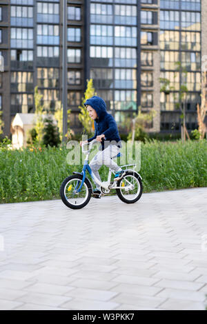 Sicherheit in einer modernen europäischen Stadt. Ein wenig glückliche junge fährt mit dem Fahrrad durch einen geschlossenen Innenhof in einem Mehrstöckigen städtischen Gebäude. Stockfoto