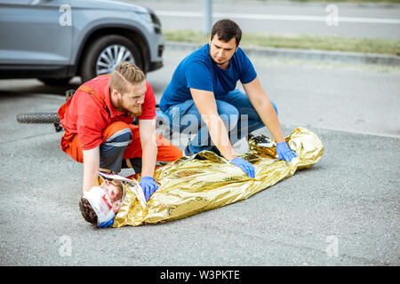 Ambluence Arbeitnehmer abdecken verletzter Mann mit thermodecke, die Notfallversorgung nach dem Verkehrsunfall Stockfoto
