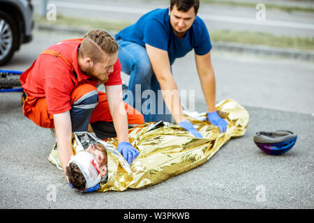 Ambluence Arbeitnehmer abdecken verletzter Mann mit thermodecke, die Notfallversorgung nach dem Verkehrsunfall Stockfoto