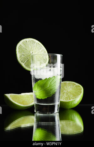 Tequila shot mit Limette, Minze und Eis auf schwarzem Hintergrund Stockfoto