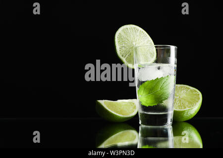 Tequila shot mit Limette, Minze und Eis auf schwarzem Hintergrund Stockfoto