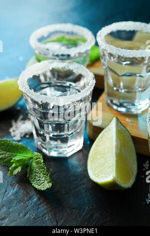 Tequila Schüsse mit Salz, Kalk Schichten und Minze auf Schwarzer Tisch mit blaues Licht Stockfoto