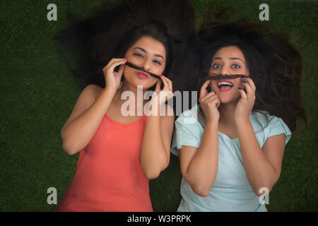 Blick von oben auf die zwei glückliche Jugend Mädchen liegen auf Gras und Schnurrbärte mit ihrem Haar Stockfoto