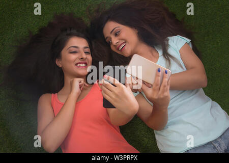 Blick von oben auf die zwei lächelnde Mädchen im Teenageralter liegen auf Gras und unter selfie mit ihren Handys Stockfoto