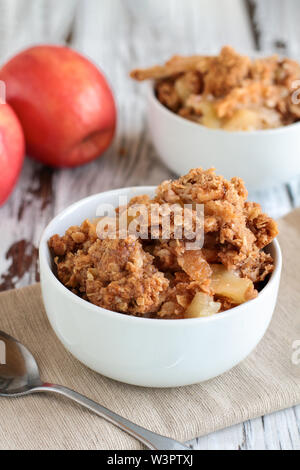 Frische heiße hausgemachte Apfel knackig oder bröckeln mit knusprigen streusel Topping in eine Schale mit frischen Äpfeln im Hintergrund gekrönt. Selektiver Fokus mit unscharfen Stockfoto
