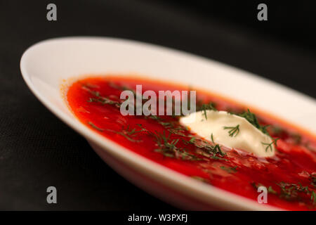 Schüssel mit Rote Beete Suppe Borschtsch mit Sauerrahm und Grüns auf schwarzen Leinwand mit dunklem Hintergrund isoliert Stockfoto