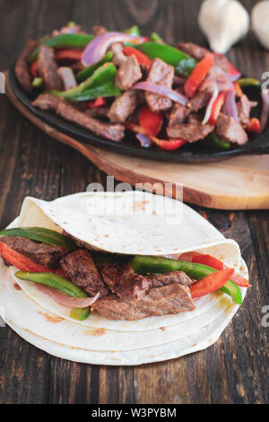 Rindersteak fajita über einem Stapel von Tortilla Wraps mit gusseisernen Pfanne mit frischem heißem fajita Mix im Hintergrund.. Selektiver Fokus mit unscharfen backgroun Stockfoto