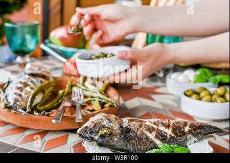 Frau mit einer Platte in den Händen. Esstisch mit verschiedenen Speisen und Snacks. Meeresfrüchte und Gemüse. Sommer Mittagessen im Freien Stockfoto
