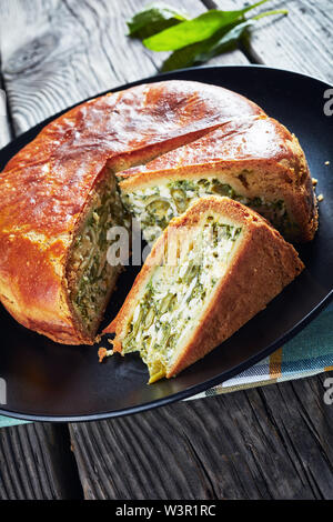 Close-up von Spinat grüne Bohne und Blue Cheese pie auf einer schwarzen Platte auf einem rustikalen Holztisch in Scheiben geschnitten, vertikale Ansicht von oben Stockfoto