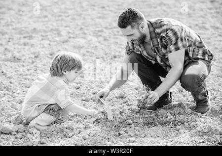 Kleiner Junge Kind helfen Vater in der Landwirtschaft. reichen natürlichen Boden. Eco Farm. Vater und Sohn Blumen Pflanzen im Boden. neues Leben. Böden, Düngemitteln. happy Earth Day. Stammbaum. Tag der Erde. Das Sitzen auf dem Boden. Stockfoto