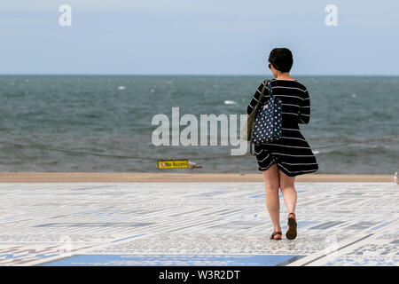 Blackpool, Lancashire. 17. Juli, 2019. UK Wetter: Hell und luftig Bedingungen in den Badeort. Es wird erwartet, später mit Regen in Bewegung aus dem Westen als Frau in einer gestreiften Kleid genießt die Witze und Zitate in der Komödie Teppich zu bewölkt. Credit: MediaWorldImages/Alamy leben Nachrichten Stockfoto