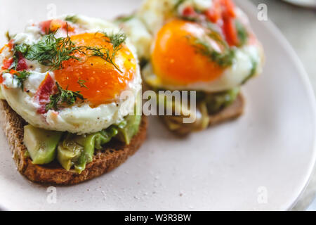Frühstück serviert von zwei Toasts mit Avocado, Spiegelei mit Gemüse und Kräutern auf einem rustikal Tischdecke Hintergrund. Blick von oben. Gesunde und Nutr Stockfoto