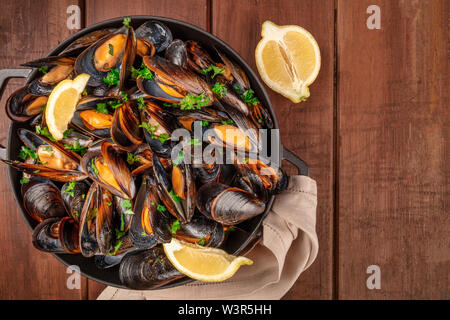 Marinara Muscheln, Moules Mariniere, mit Zitronenscheiben, in einem Kochtopf, Schuß von der Oberseite in einem dunklen Holzmöbeln im Landhausstil Hintergrund mit Kopie Raum Stockfoto