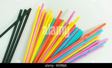Mehrfarbige plastik Trinkhalme und ein Paar schwarze Papier Trinkhalme verteilen sich auf eine neutrale Oberfläche, einfache Benutzung von flexible Trinkhalme Stockfoto