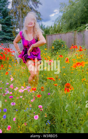 Blonde Frau tanzen in Ihrem Hinterhof voller Wildblumen. Stockfoto