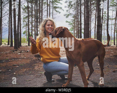 Lächelnden jungen Frau das Spielen mit Ihrem Hund im Wald Stockfoto