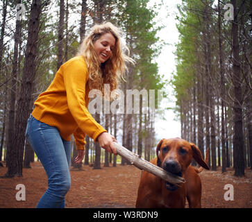 Blonde junge Frau und ihr Hund spielt mit Stick Stockfoto