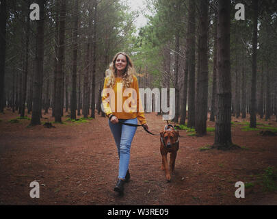 Junge blonde Frau, gehen mit Ihrem Hund im Wald Stockfoto