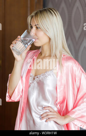 Eine junge schöne blonde Mädchen morgens aufwacht und Wasser trinkt. Stockfoto