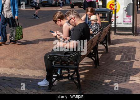 Zwei Männer, Chillen und auf ihren Handys sitzen auf einer Bank in Abington st, Northampton, Großbritannien. Stockfoto