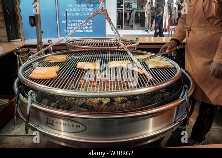 Große runde Grill mit Bratwurst Würstchen grillen auf der Grillplatte auf dem Deutschen Weihnachtsmarkt in Birmingham, Großbritannien Stockfoto