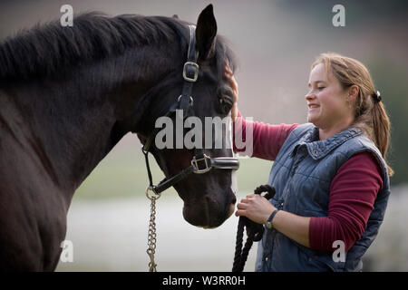 Junge Frau schwarzes Pferd Streicheln auf der Nase. Stockfoto