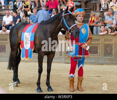 Ein Mann, der mittelalterlichen Kostüm steht mit seinem Pferd auf der Rennstrecke an der Palio jährliche Veranstaltung in Siena, Italien Stockfoto