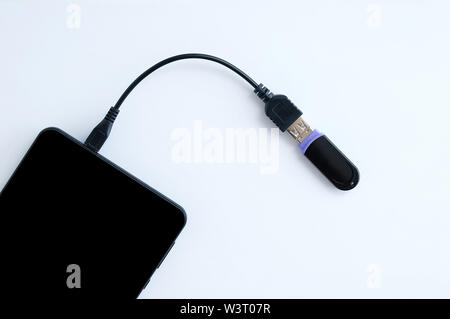 Übertragen Sie digitale Daten. Das Kabel ist an das Smartphone und USB-Flash-Laufwerk angeschlossen ist. Weißer Hintergrund. Stockfoto