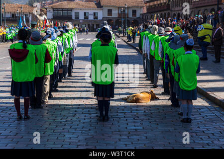 Peruanische Hund schlafen auf der gepflasterten Straße, umgeben von einer Gruppe von Schulkindern auf der Parade in der Plaza de Armas, dem Hauptplatz, Cusco, Peru, Südafrika Stockfoto