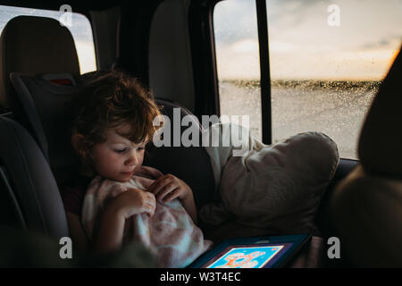 Junge Mädchen spielen Lernspiel auf der Fahrt mit dem Auto nach Hause, während es regnet Stockfoto