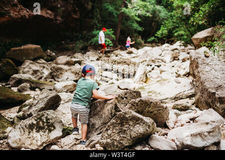 Junge Felsen klettern, mit Vater und Schwester zu fangen beim Wandern Stockfoto