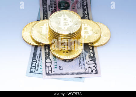 Ein Haufen Gold farbigen Bitcoins auf $ 50 und $ 100 US-Währung Rechnungen isoliert. Stockfoto