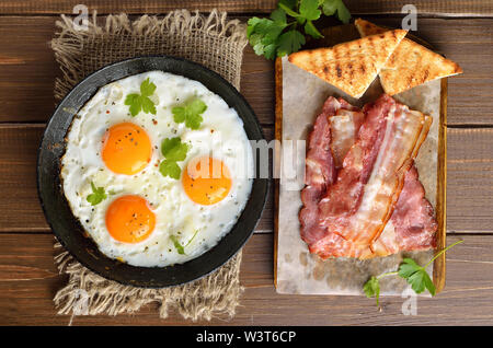 Gebratene Eier, Speck und Toast auf Schneidebrett. Ansicht von oben, flach Stockfoto