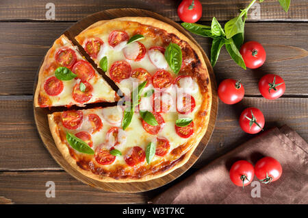 Appetitliche Pizza Margherita auf einem schneidebrett, frische Tomaten und Basilikum auf hölzernen Tisch. Ansicht von oben, flach Stockfoto