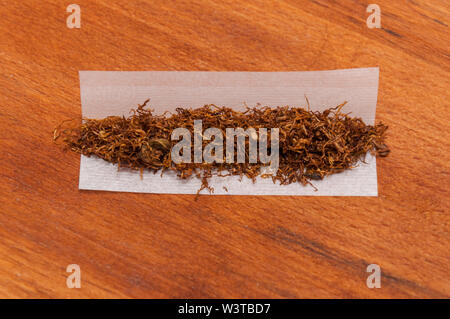 Hand Rolling Paper mit Tabak auf den braunen Holz Stockfoto