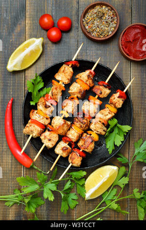 Gegrilltes Hühnchen Kebab mit Paprika in der Pfanne, Gemüse und Kräutern auf Holztisch, Ansicht von oben Stockfoto