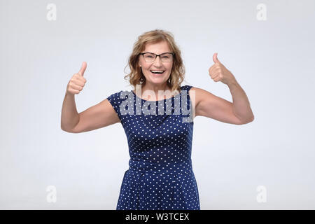 Lächelnd hübsche reife Frau, Daumen nach oben. Studio gedreht. Positive facial menschliches Gefühl. Stockfoto
