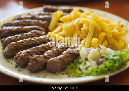 Cevapi, traditionelle serbische Spezialität mit Pommes frites, Salat und Zwiebeln Stockfoto