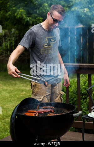 Ein junger Mann kocht Bratwurst und Hot Dogs auf seinen Grill in der im Hinterhof seines Lawrence, Indiana. Stockfoto