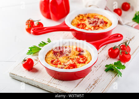 Frittata mit frischen süßen Paprika, Tomaten und Salami. Italienische Omelette in rot Keramik skillets auf einem weißen Hintergrund. Nahaufnahme Stockfoto