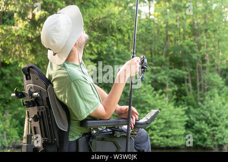 Glücklicher Mann in einem elektrischen Rollstuhl werfen Angel am schönen Teich in der natue an einem sonnigen Tag Stockfoto