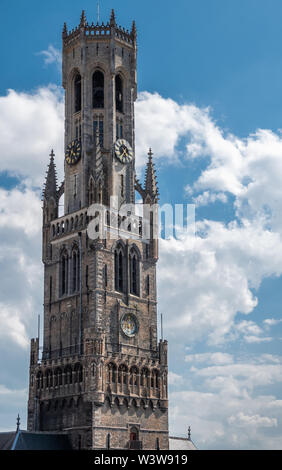 Brügge, Flandern, Belgien - 17 Juni, 2019: Nahaufnahme von Glockenturm hoch Grau brick Clock Tower, Halletoren, gegen den blauen Himmel mit weißen Wolken. Stockfoto