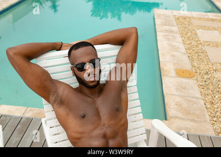 Mann in Sonnenbrille entspannen Sie sich auf einem Liegestuhl in der Nähe von Schwimmbad Stockfoto